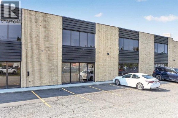 Side exterior of a commercial building with large windows and parked cars. - 13, 4063 74 Avenue Se, Calgary