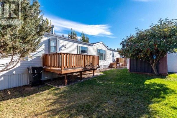 Rear exterior of a white mobile home with a wooden deck and green lawn. - 13, 5302 56b Street, Lloydminster
