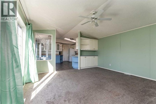 Living room with grey carpet, pale green walls, built-in cabinets, and a ceiling fan. - 13, 5302 56b Street, Lloydminster