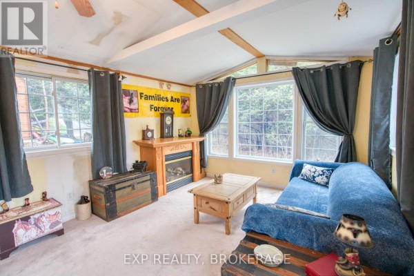 Living room fireplace with wood mantel, electric insert, and large windows with trees outside. - 13 - 1014 Teal Trail, Frontenac