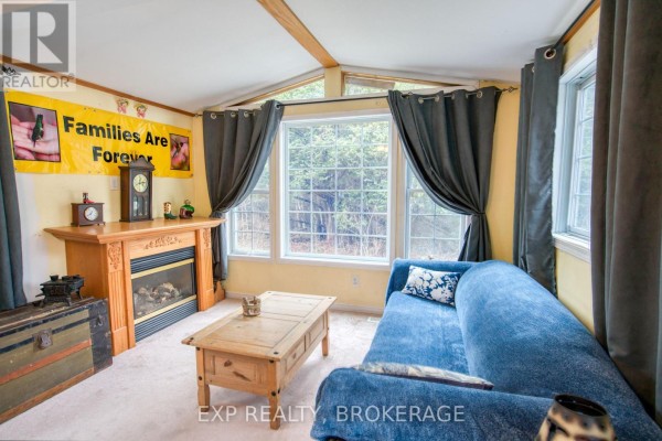 Living room with a blue sofa, fireplace, and wooden coffee table looking out large windows. - 13 - 1014 Teal Trail, Frontenac