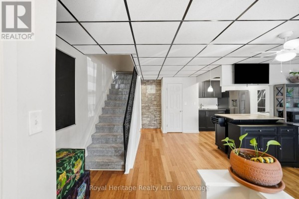 Open-concept living area with staircase, stone wall, dark cabinets, and island. - 13 - 162 Cromwell Street, Trent Hills