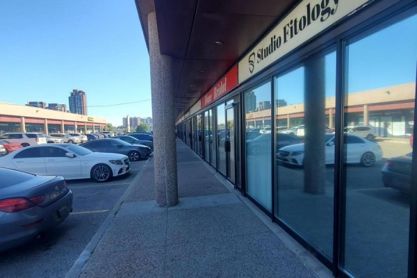 Exterior view of a retail strip with a parking lot, featuring storefronts with reflective glass windows. - 13 - 3220 Dufferin Street, Toronto