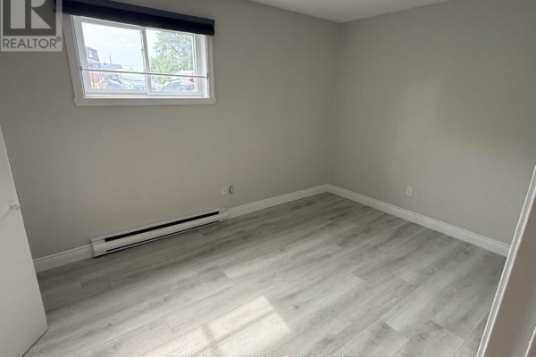 Empty room with light grey walls, light wood laminate flooring, and a window overlooking houses. - 3 - 65 Race Street, Cornwall