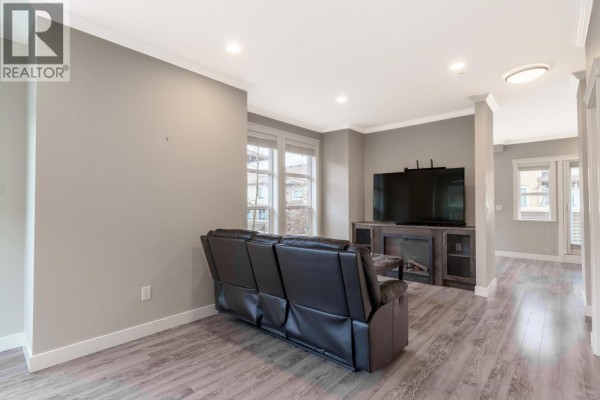 Living room with dark leather sofa, coffee table, and large windows with natural light - 13 10550 248 Street, Maple Ridge