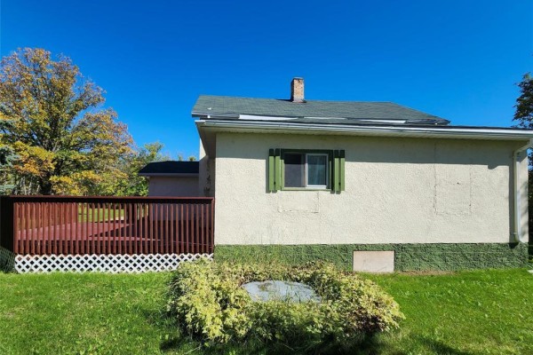Rear side of the house with a large wooden deck and lattice skirting. - 13 1st Street N, Eriksdale