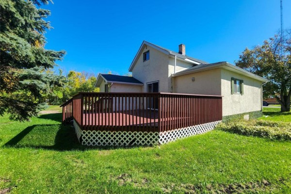 Exterior view of the house featuring a spacious wooden deck and green lawn. - 13 1st Street N, Eriksdale