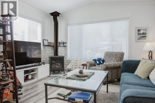 Living room with a blue sofa, patterned armchair, glass coffee table, and a black gas fireplace. - 13 4496 Sunshine Coast Highway, Sechelt