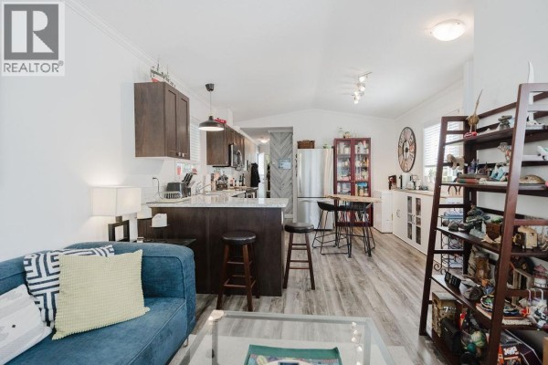 Open concept living room and kitchen with dark wood cabinets, stainless steel appliances, and seating. - 13 4496 Sunshine Coast Highway, Sechelt