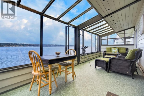 Sunroom with large windows offering ocean views, featuring wicker furniture and a dining set. - 13 523 Island Hwy, Campbell River