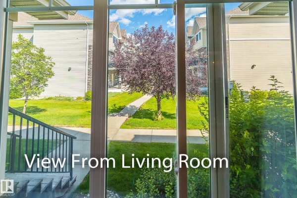 View through glass doors to a green lawn and townhouses with trees in summer. - #13 7289 South Terwillegar Dr Nw, Edmonton
