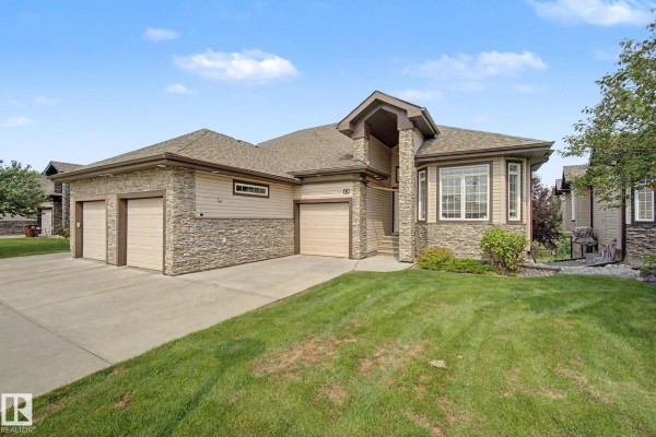 Two people walking on a paved path beside a duplex building and evergreen trees. - #13 85 Northridge Dr, St  Albert