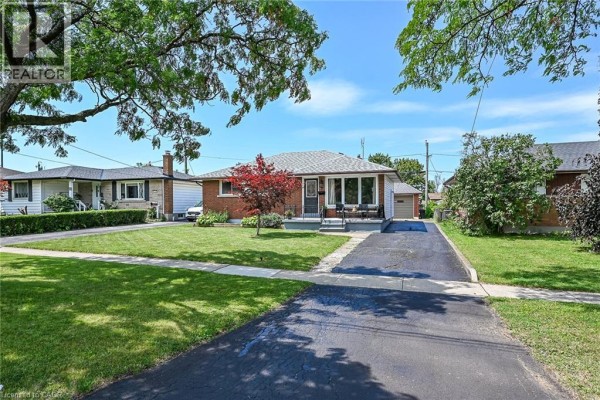 Wide shot of the brick bungalow from across the street, showing the manicured lawn and mature trees. - 13 Allanburg Road S, St  Catharines