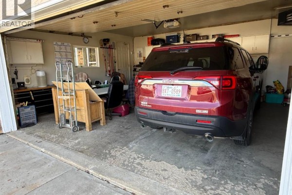 Another view of the garage interior, detailing a workbench, red SUV, and storage. - 13 Assiniboine Drive, Swan Hills