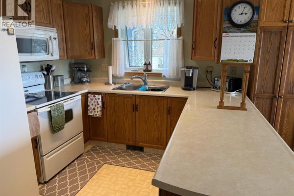 Kitchen view with white appliances, oak cabinets, light countertops, and a window above the sink. - 13 Assiniboine Drive, Swan Hills