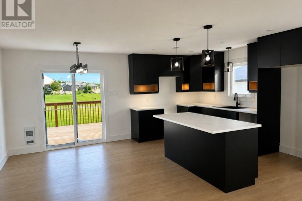 Modern open-concept kitchen with black cabinets, white quartz countertops, and a large island. - 13 Blandford Street, Gander