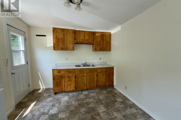 Kitchenette with light wood cabinets, white countertops, and a double sink below a window. - 13 Chester Avenue, Kentville