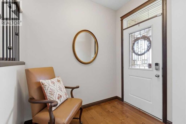 Foyer area with a white door, ornate mirror on the wall, and a leather armchair with a patterned cushion. - 13 Cranford Gardens Se, Calgary