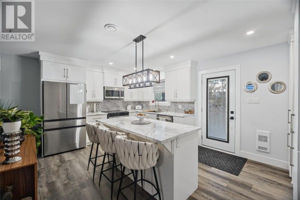 Open concept living and kitchen area with white cabinets, marble island, and grey sofa. - 13 Kimbar Drive, Conception Bay South