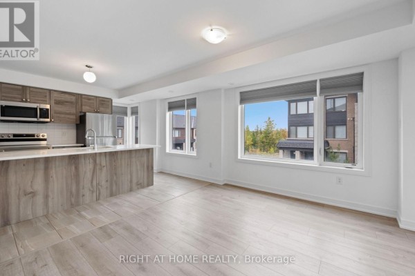 Open concept kitchen and living area with stainless steel appliances, island, and large windows. - 13 Magnolia Lane, Barrie