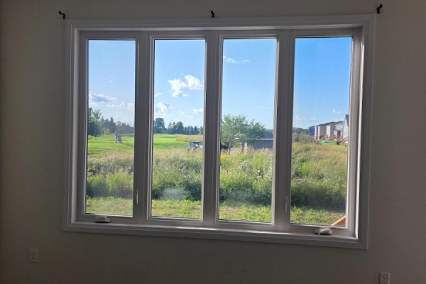 Large white window frame with four panes showing a sunny green field and construction in the background. - 13 Oakmont Drive, Loyalist