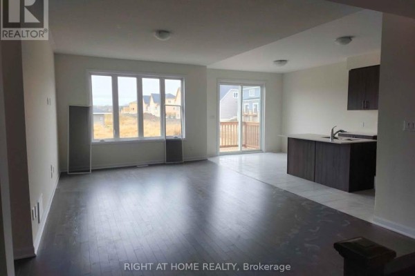 Open concept living and dining area with dark hardwood floors, large window, and sliding glass doors to deck. - 13 Oakmont Drive, Loyalist