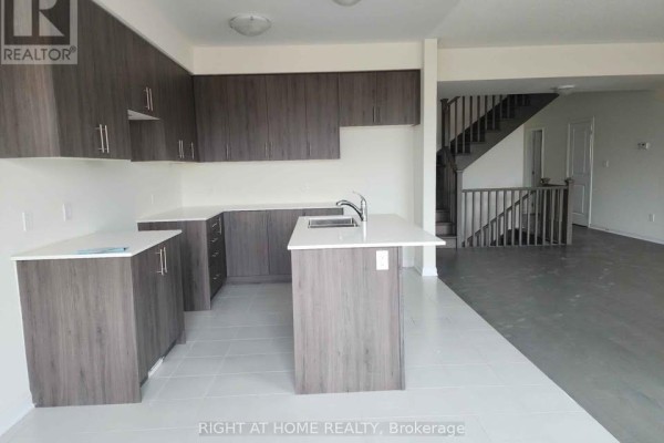 Modern kitchen with dark wood cabinets, white countertops, island with sink, and view of staircase. - 13 Oakmont Drive, Loyalist