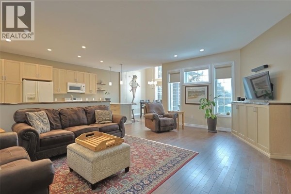 Living room with a dark brown sofa, patterned rug, hardwood floors, and large windows. - 13 Oakwood Links Lane, Grand Bend