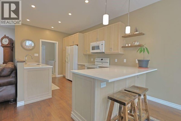 Kitchen with light wood cabinets, a white island with two stools, and stainless steel appliances. - 13 Oakwood Links Lane, Grand Bend