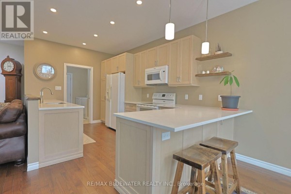 Kitchen with light wood cabinets, white appliances, a breakfast bar, and pendant lights. - 13 Oakwood Links Lane, South Huron