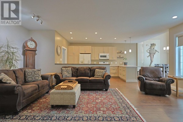 Living room with dark brown sofas, a patterned rug, and an open view to the kitchen. - 13 Oakwood Links Lane, South Huron