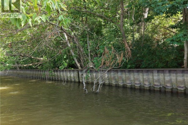 Waterfront view of a weathered wooden retaining wall bordering a treed area. - 13 Quay Street, Port Dover