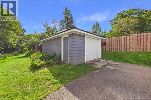 A detached grey garage with a white garage door and a wooden fence behind it. - 13 Squire Street, Sackville