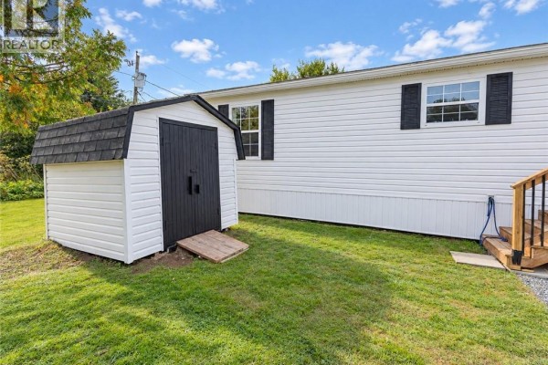 Side view of the white mobile home and a detached white shed with a black roof on a grassy lawn. - 13 Wood Avenue, Lincoln