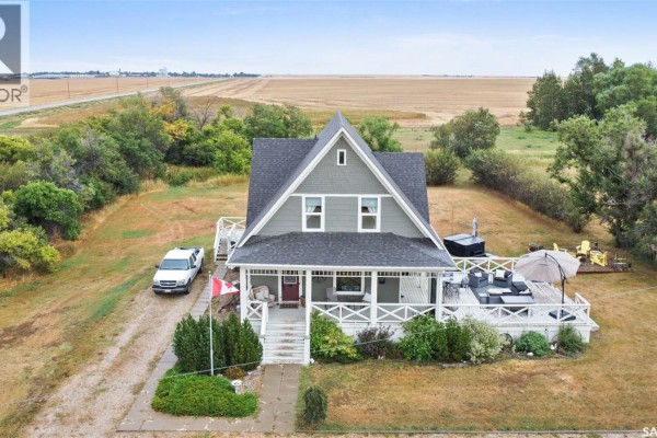 Aerial view of a light grey house with a wrap-around porch, hot tub, and surrounding rural landscape. - 13.04 Acreage By Lake Diefenbaker, Canaan Rm No  225