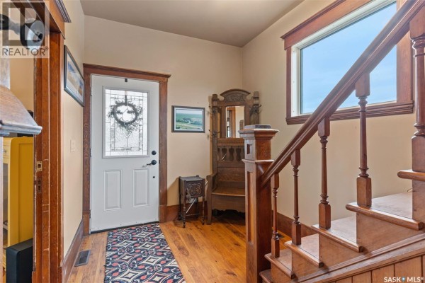Interior entryway with a white door, wooden staircase, antique bench, and patterned rug. - 13.04 Acreage By Lake Diefenbaker, Canaan Rm No  225