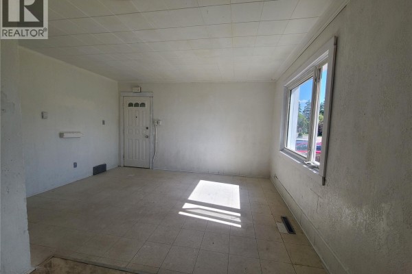 Living room with white walls, tiled floor, and a large window overlooking the street. - 130 26th Street W, Prince Albert