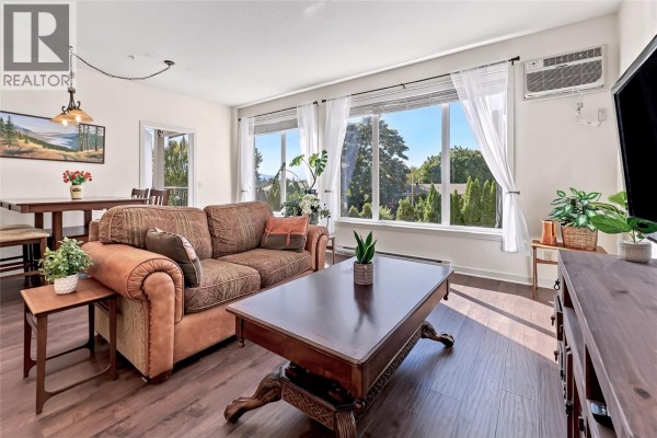 Living room with large windows, a couch, and a dining table in the background. - 130 Barber Road Unit# 103, Kelowna