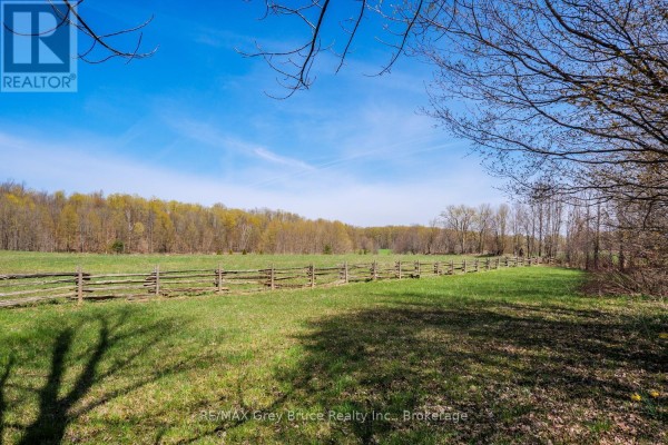 A wide, green grassy field with a rustic wooden fence running along the horizon. - 130 Crooked Hill Road, South Bruce Peninsula