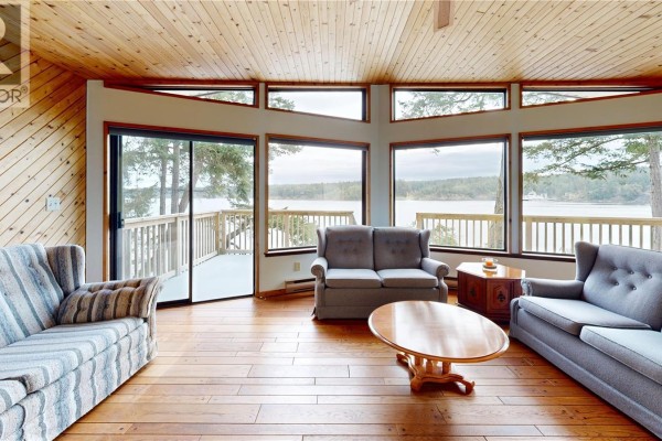 Living room with wood-paneled walls and ceiling, large windows, and water view. - 130 Easthom Rd, Gabriola Island