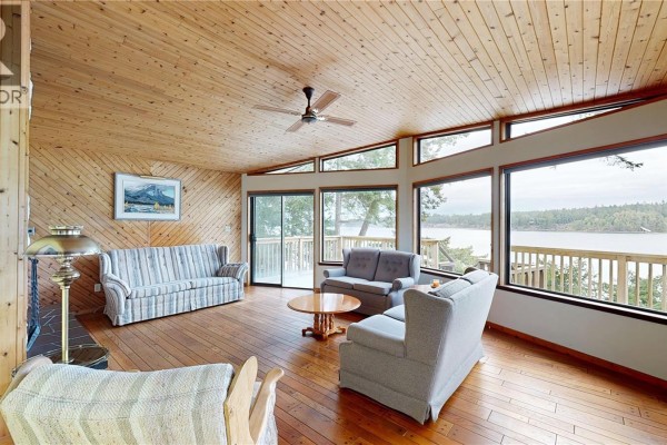 Living room with wood-paneled walls and ceiling, sofa, armchairs, and water view. - 130 Easthom Rd, Gabriola Island