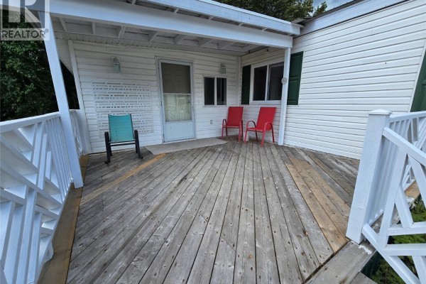 View of the wooden deck on the covered porch with two red chairs and one teal chair. - 130 Ferry Road Unit# 7, Clearwater