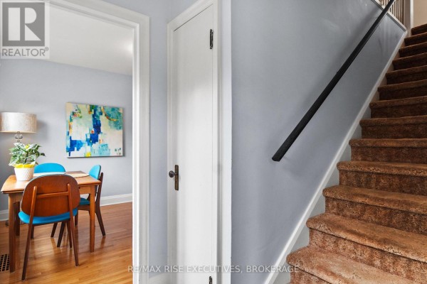 Hallway with stairs leading up, a white door, and a dining area visible through a doorway. - 130 Florence Street, Kingston