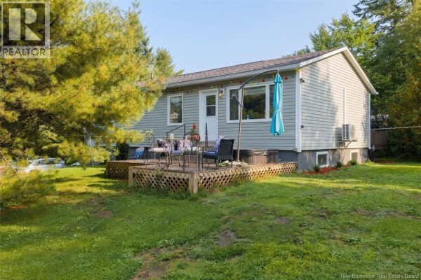 Side view of a grey vinyl-sided house with a sloped lawn, garden beds, and a lighthouse decoration. - 130 Hillcrest Road, Saint John