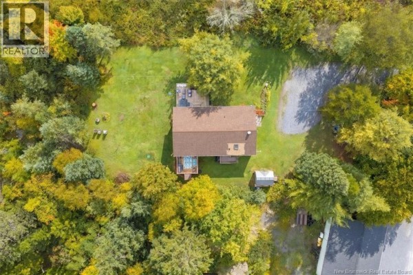 Aerial view of a house surrounded by trees and green lawn, with a deck and shed. - 130 Hillcrest Road, Saint John