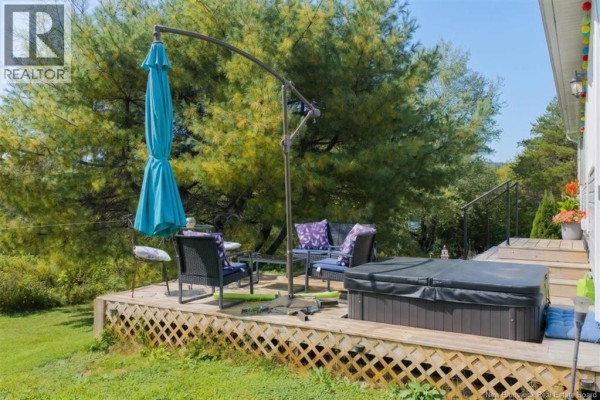 Close-up view of a wooden deck with a hot tub, patio furniture, and a large blue umbrella. - 130 Hillcrest Road, Saint John