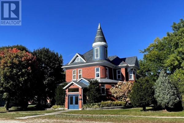 Side angle of a red brick residence featuring a blue turret, dormer windows, and manicured shrubs. - 130 John Street, North Perth