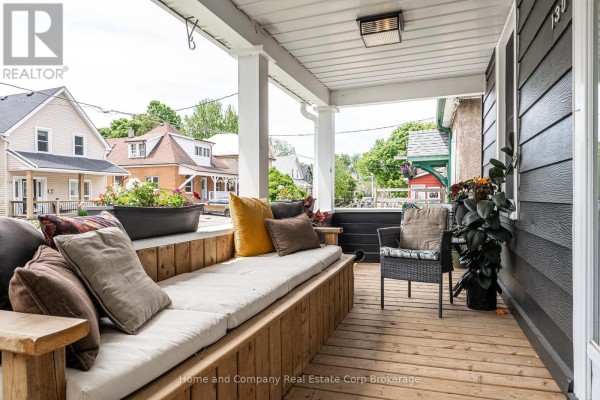 Covered wooden porch with built-in seating, cushions, and chairs, overlooking a street. - 130 Rebecca Street, Stratford