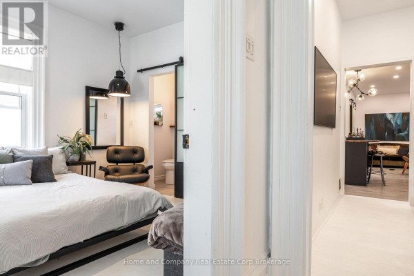 Bedroom with a large bed, black leather chair, and a view into a hallway and bathroom. - 130 Rebecca Street, Stratford