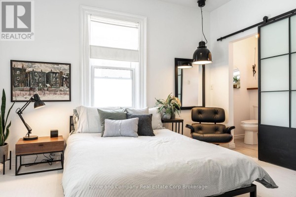 Bedroom with a large bed, bedside table, black chair, and a view of a sliding barn door. - 130 Rebecca Street, Stratford
